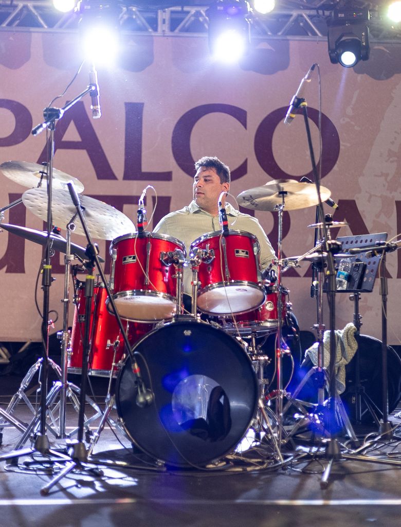 Eduardo Pirajá na bateria vermelha em palco, com microfones suspensos
