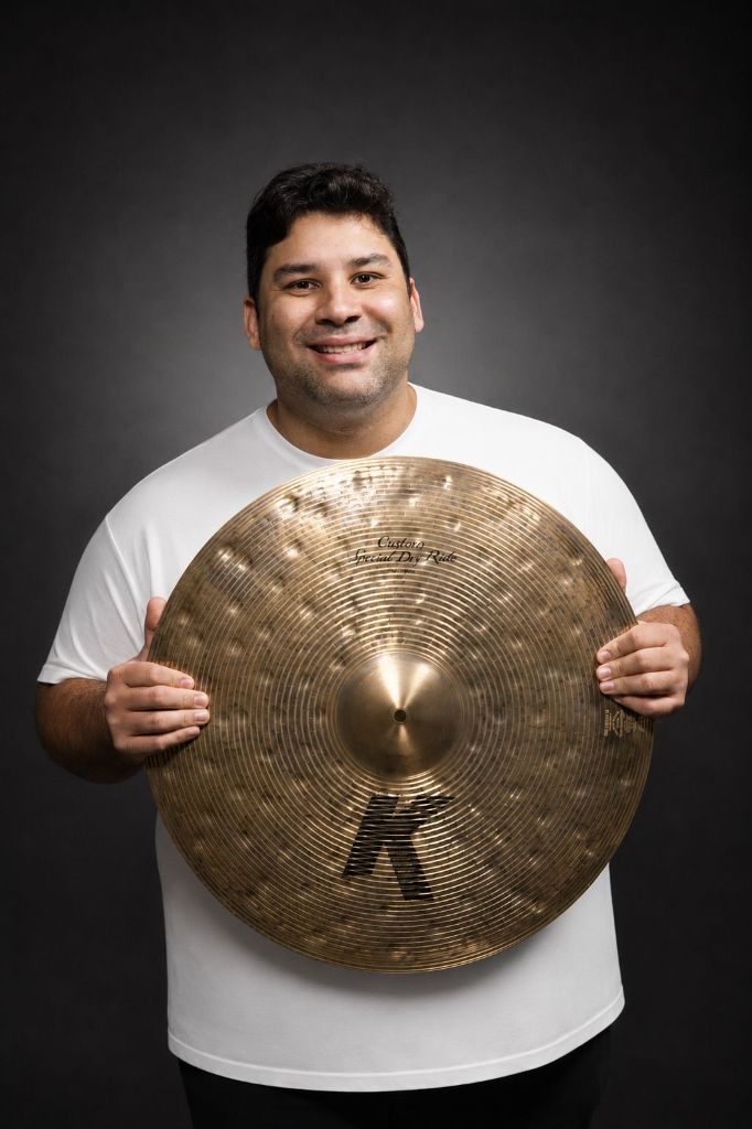 Retrato de Eduardo Pirajá, baterista e educador musical, segurando um prato de bateria